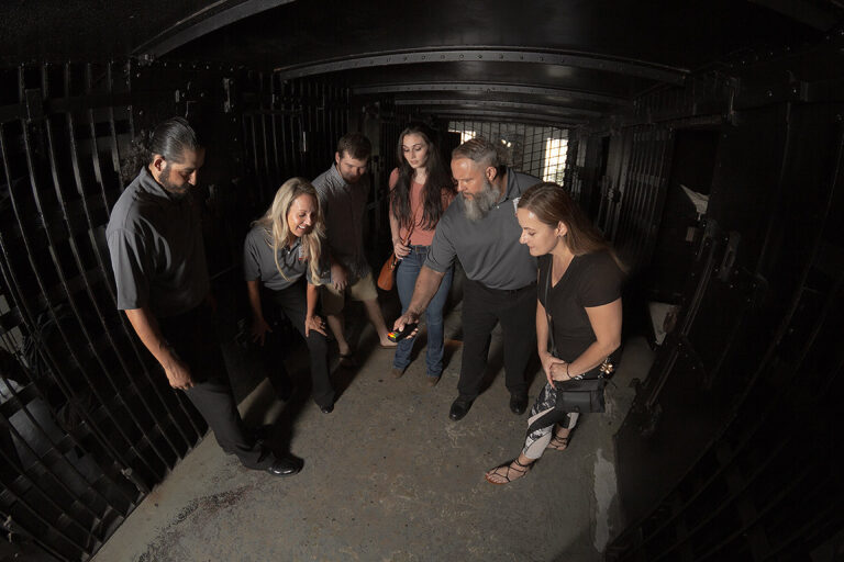 guests and tour guides standing around inside a cell at the St. Augustine Old Jail and they're all looking at an EMF meter held by one of the guides